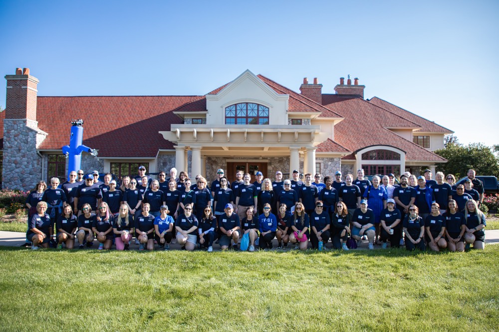 Group of GVSU Alumni Move in day volunteers take a group picture in front of Alumni House and Visitors Center
